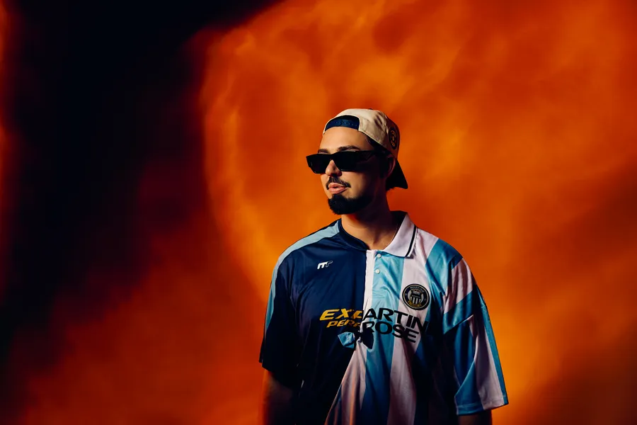 Sonny Fodera in sunglasses and a football shirt against a fiery orange backdrop
